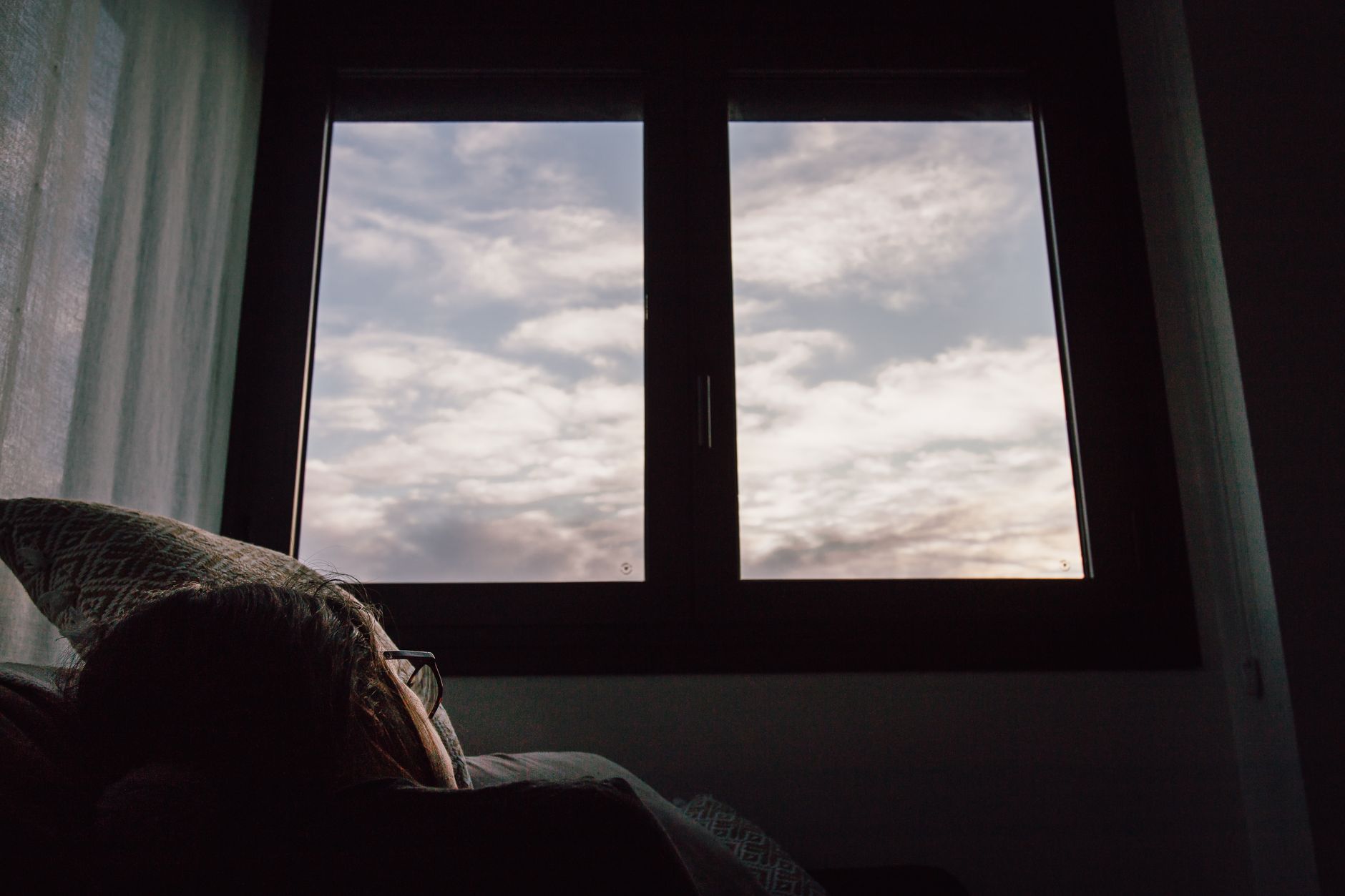 A serene view of the sky with clouds through a window, witnessed from a cozy bedroom setting