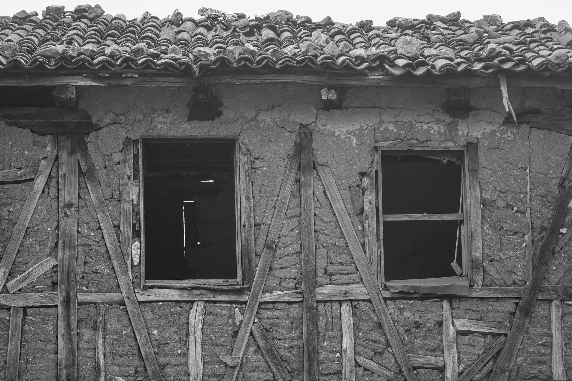 A black and white photo of an old, rundown house with wooden beams and two empty window frames